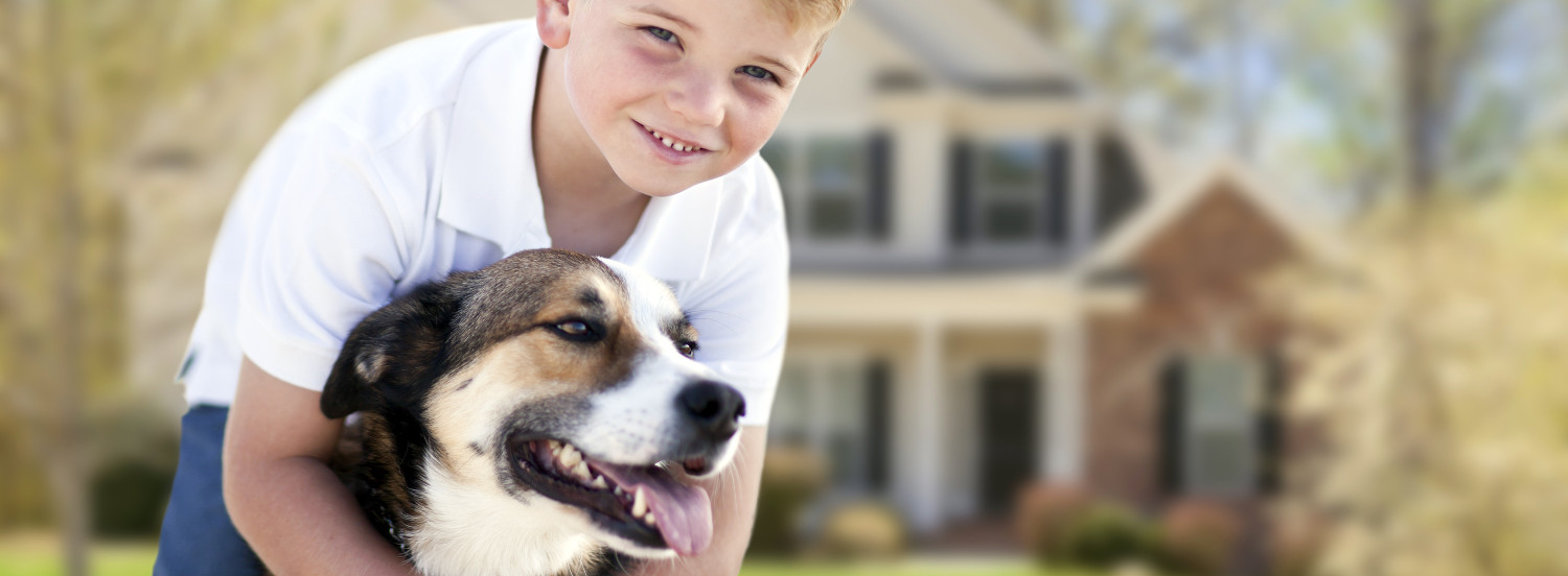 Photo of a boy and dog in front of a house.